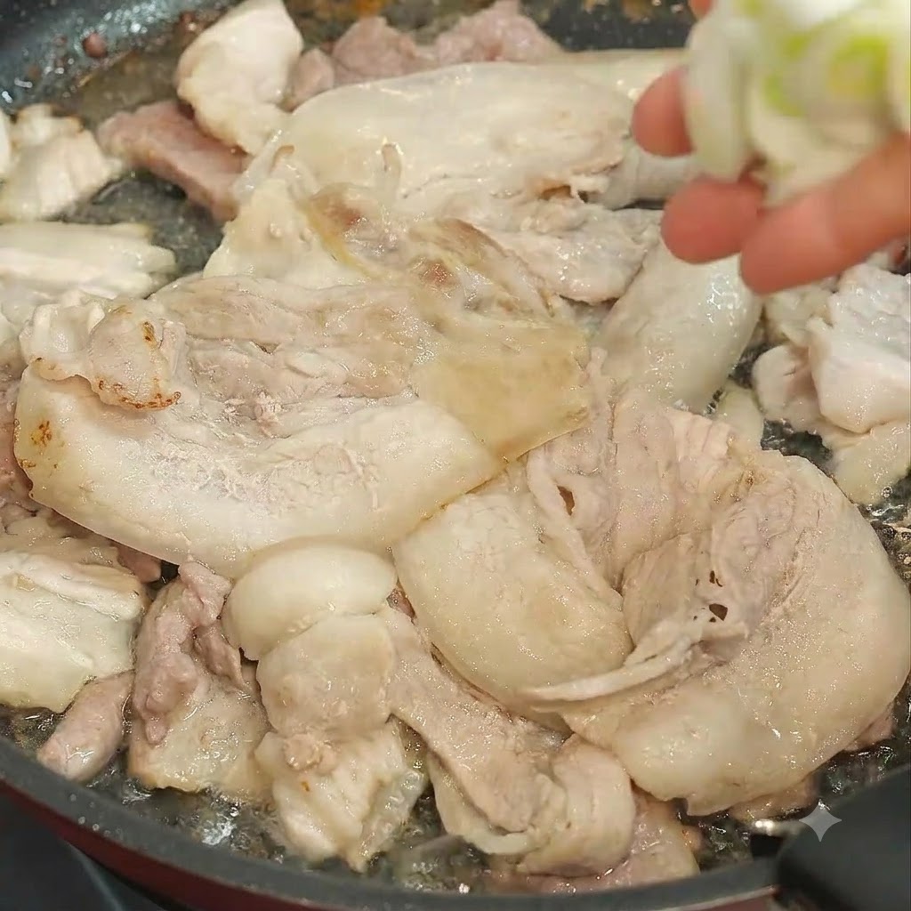 Eine Hand wirft gehackte Frühlingszwiebeln in eine Pfanne mit braten den Schweinefleischscheiben.