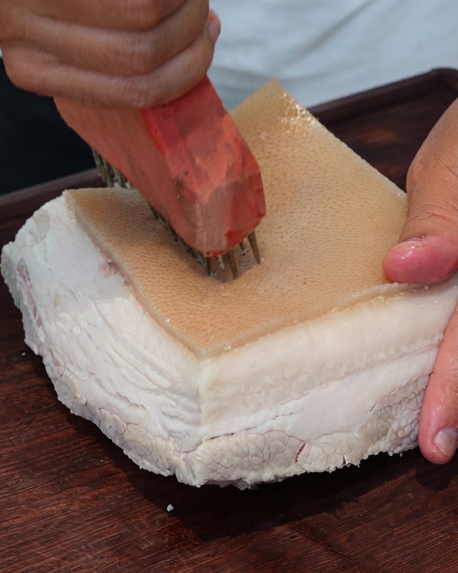 Nahaufnahme eines Fleischpikierwerkzeugs, das wiederholt Löcher in die Oberfläche der Schweinehaut sticht.