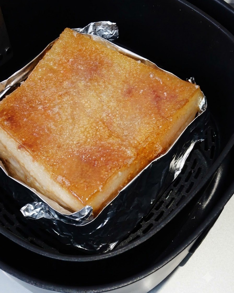 Der geröstete Schweinebauch liegt im Heißluftfritteusenkorb, wobei seine gesalzene Haut goldbraun gebacken ist.