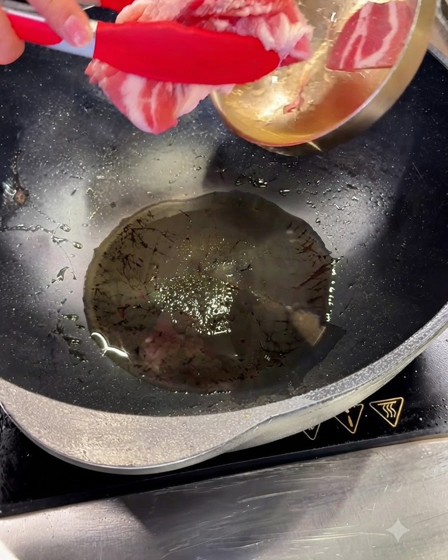 Schweinebauchscheiben werden mit roten Zangen in heißes Öl in einem Wok gegeben.