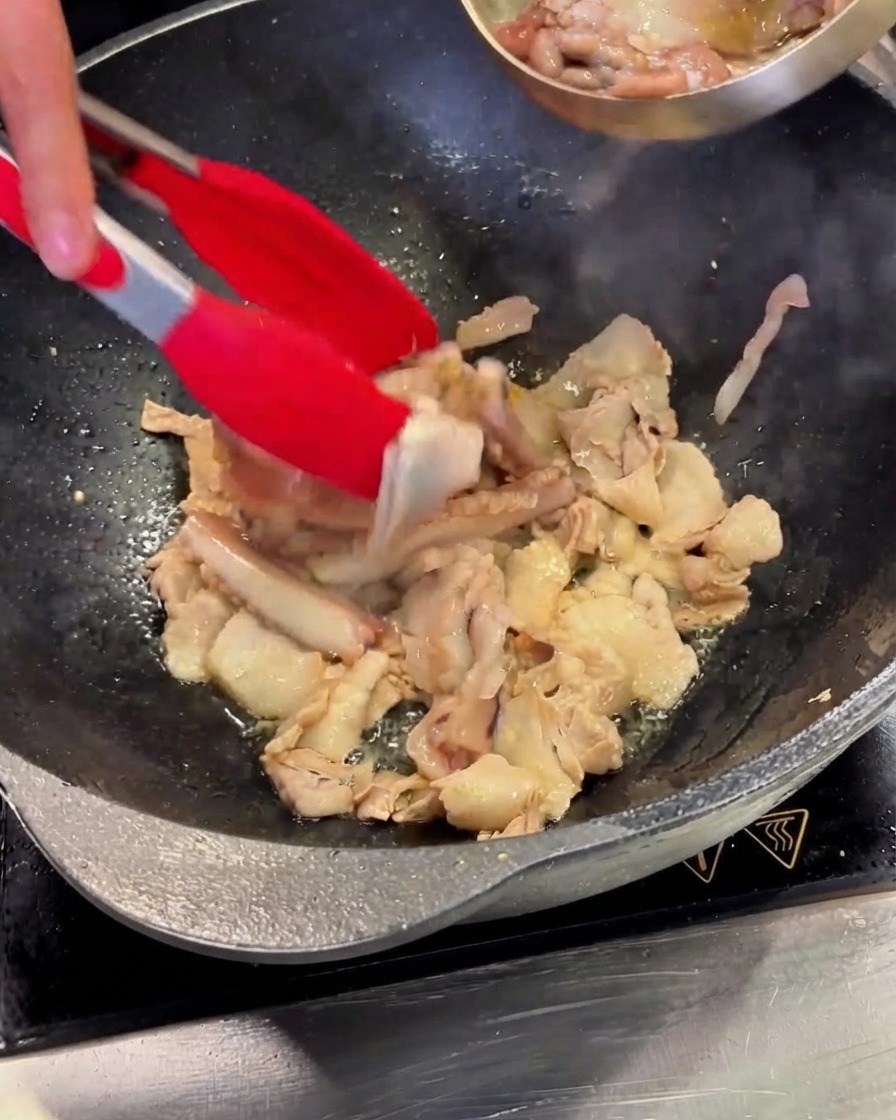 Gereinigte Tintenfischstücke werden aus einer Stahlschüssel in den Wok mit Schweinebauch geschüttet.
