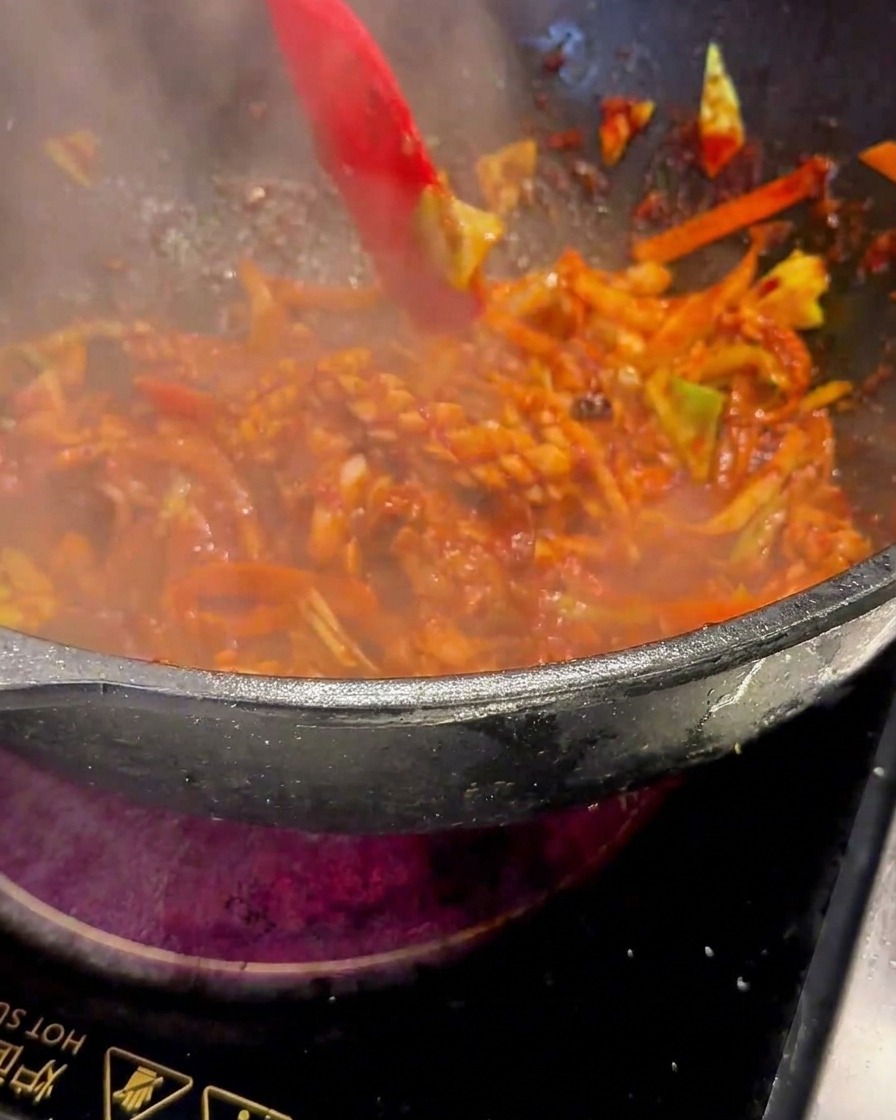 Ein roter Spatel rührt die brutzelnde Mischung im Wok bei starker Hitze um.