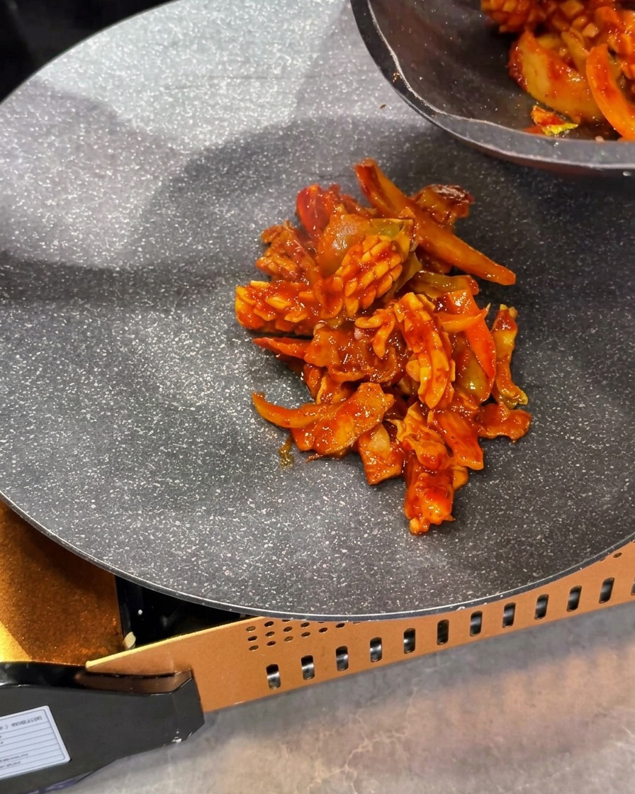 Die gekochte rote Tintenfisch-Schweinefleisch-Pfannenmischung wird in die Mitte einer Pfanne auf einem tragbaren Gaskocher gegeben.