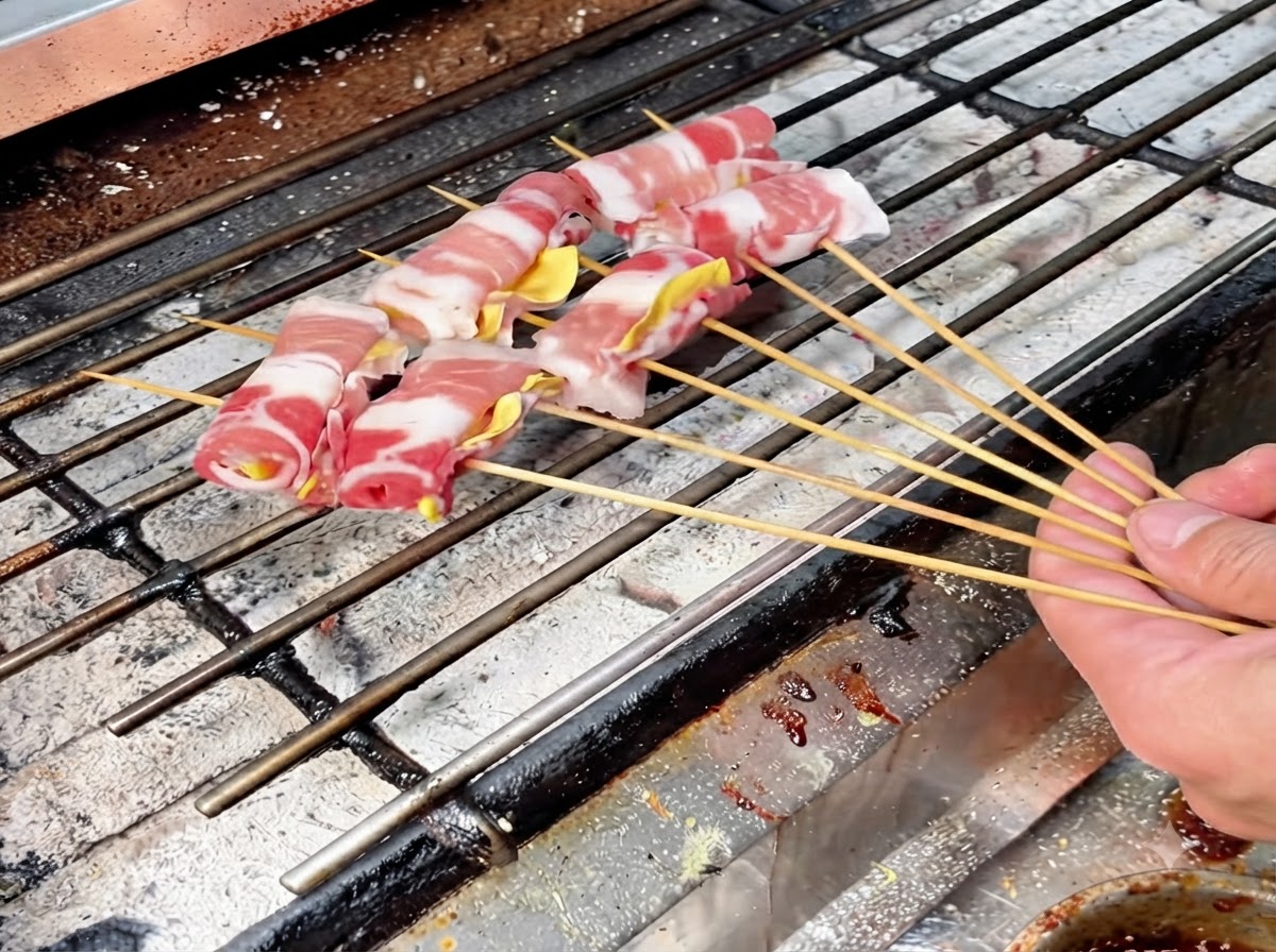 Mehrere aufgespießte Fleischrollen auf einem heißen Holzkohlegrillrost zum langsamen Braten angeordnet.