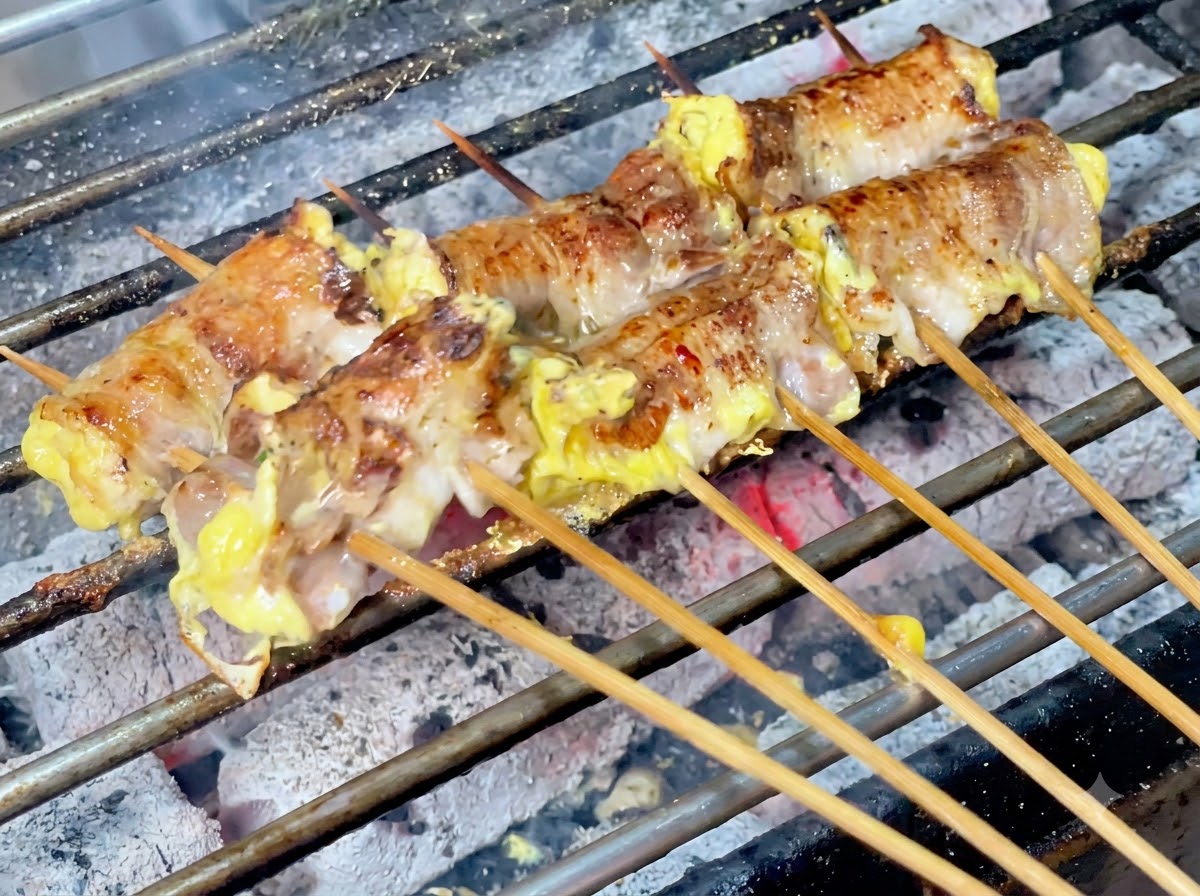 Chilipulver wird über die zischenden Fleischrollen auf dem Holzkohlegrill gestreut.
