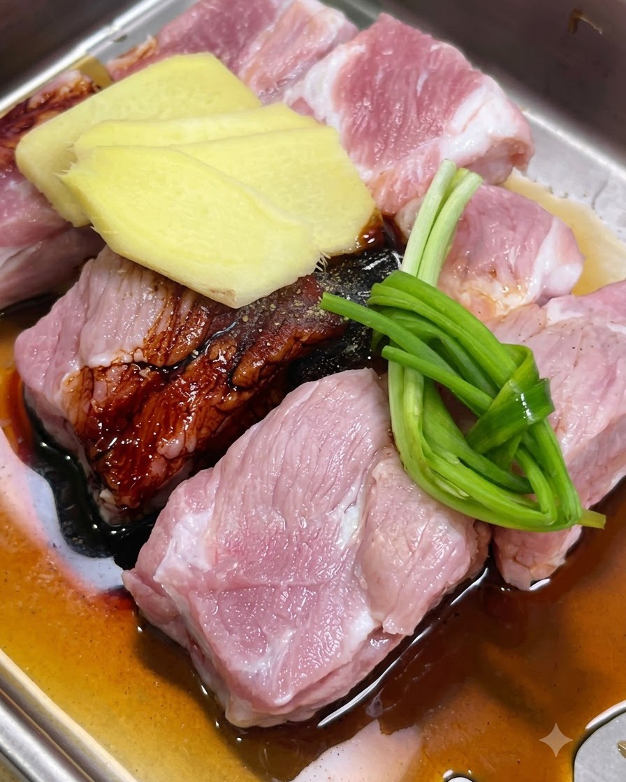 Schweinerippchen werden in einer Schale mit Ingwerscheiben, Frühlingszwiebeln und Saucen mariniert.