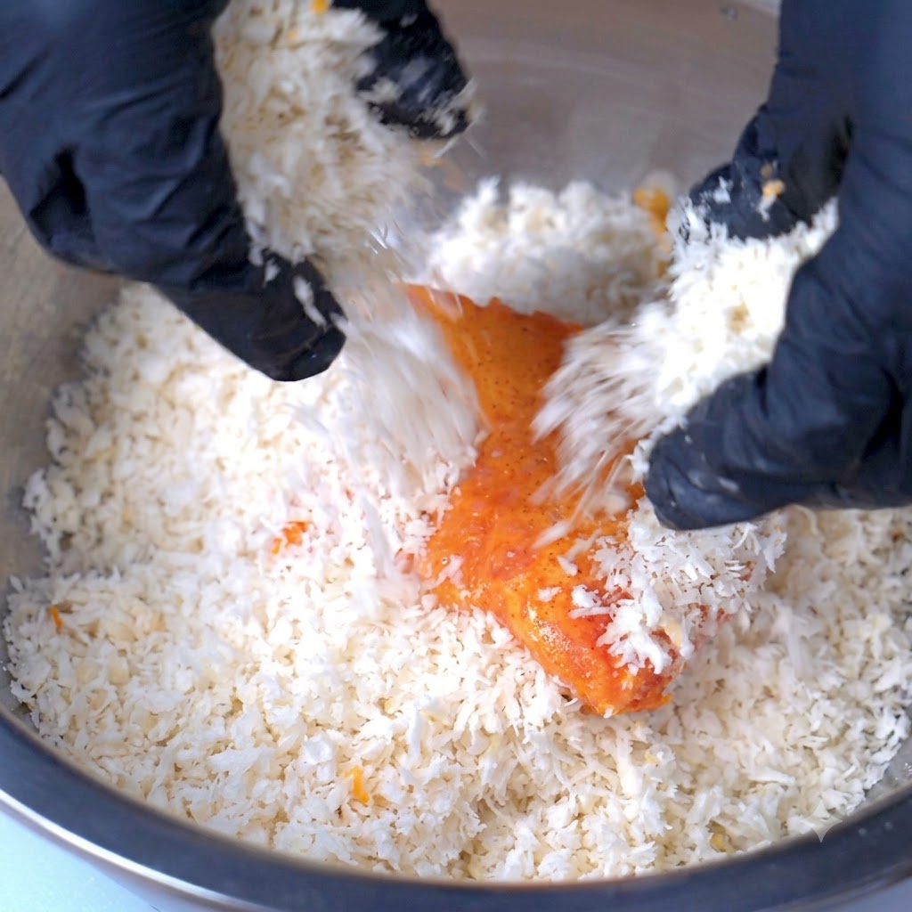 Ein Schweineschnitzel wird in einer großen Schüssel mit einer dicken Schicht Paniermehl bedeckt.