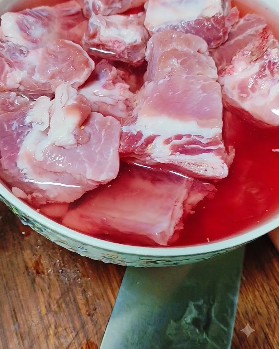 Rohe Schweinerippchen weichen in einer Schüssel mit rötlich gefärbtem Wasser ein.