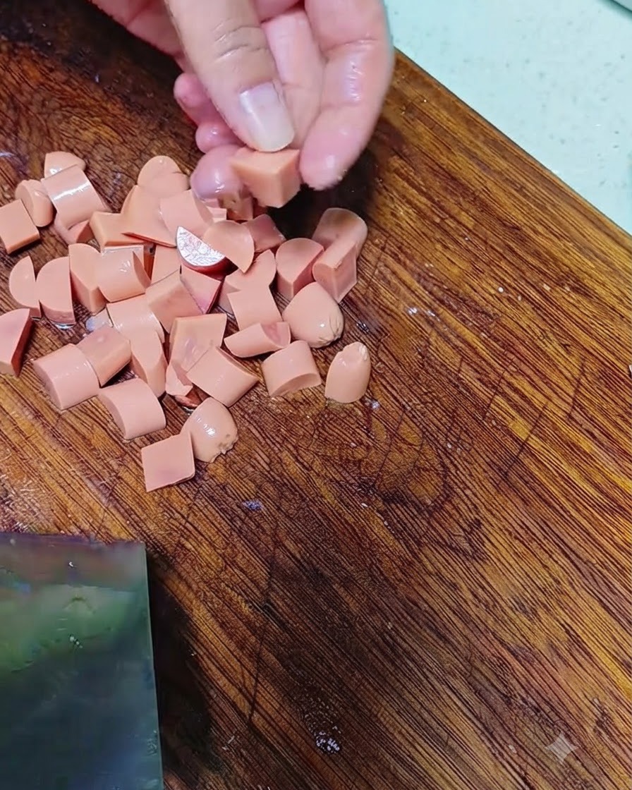 Hände schneiden Wurst auf einem Holzschneidebrett in kleine Stücke.