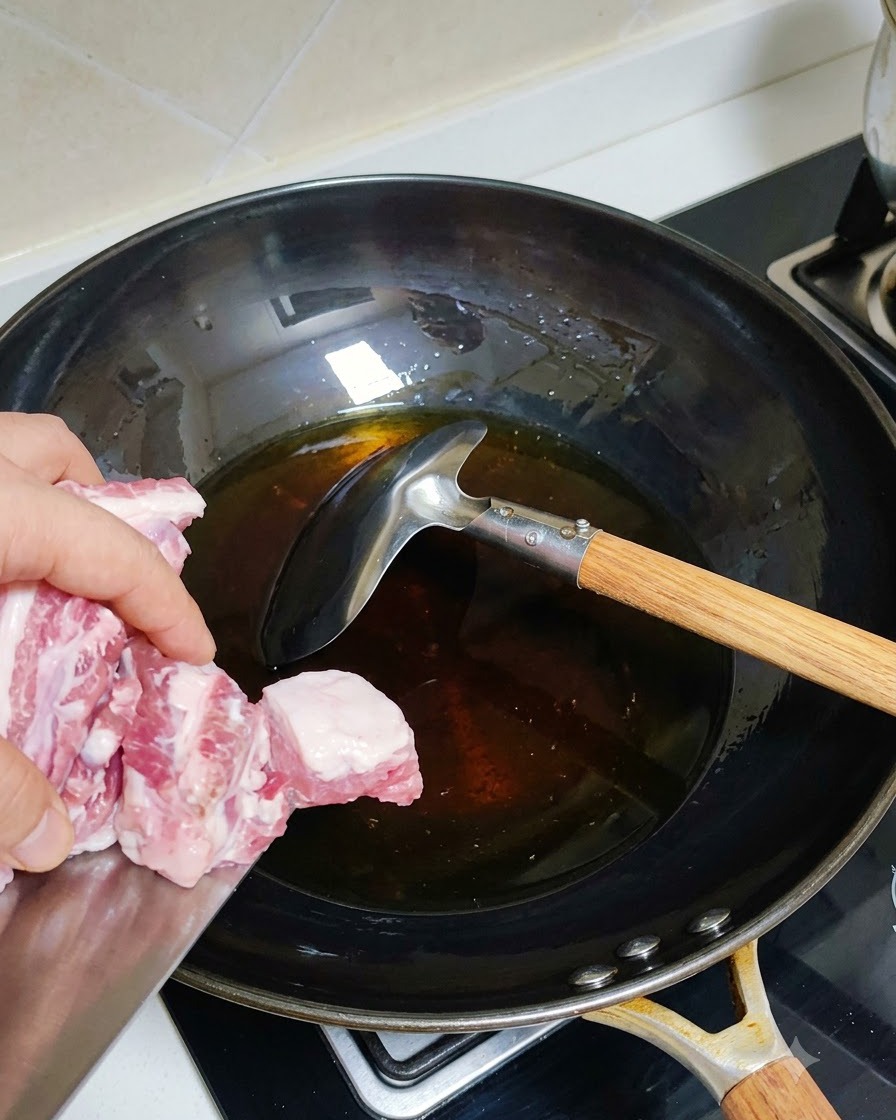 Blanchierte Schweinerippchen werden in einen heißen Wok mit Öl gegeben.