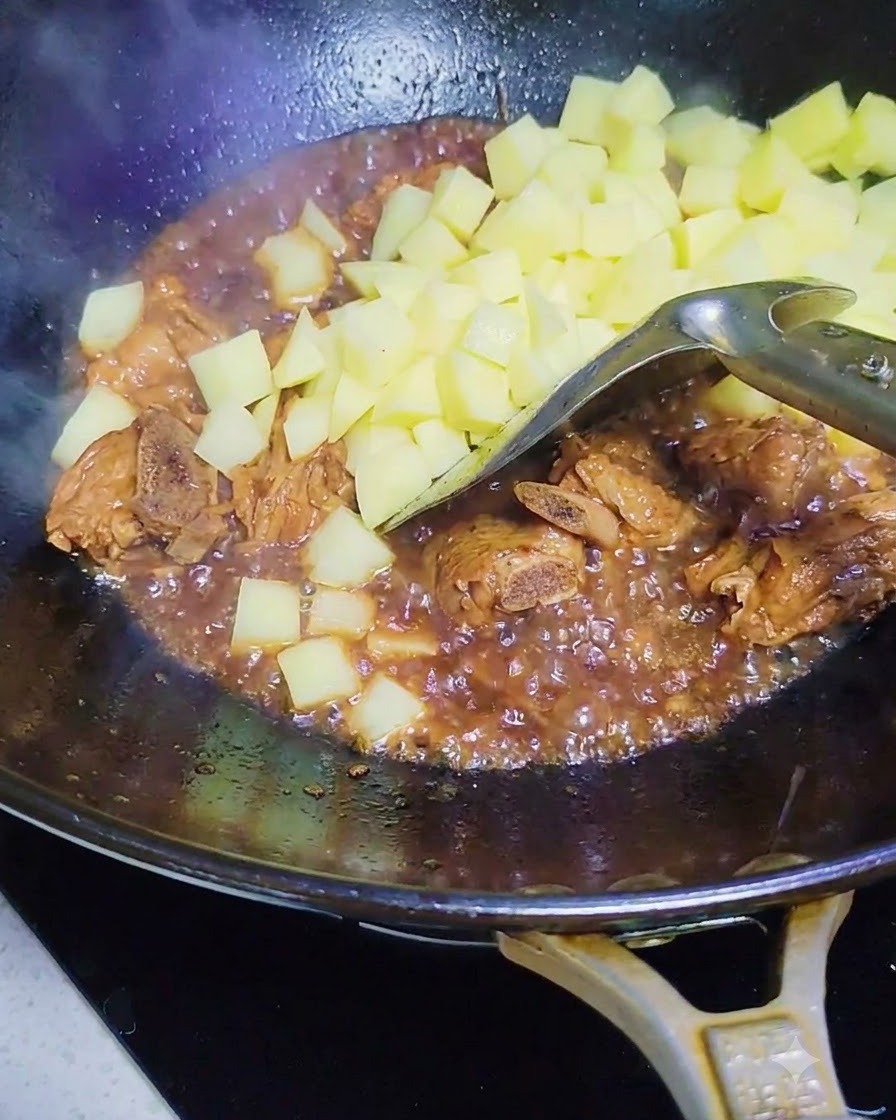 Rohe Kartoffelwürfel werden in den Wok mit den Schweinerippchen und der Sauce gegeben.