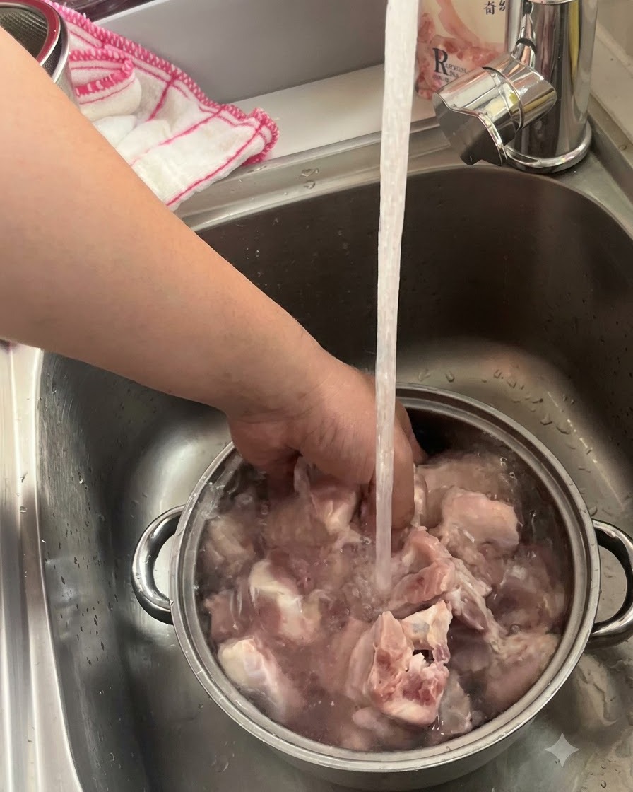 Schweinerippchen, die in einer Metallschüssel unter einem laufenden Küchenwasserhahn eingeweicht und gewaschen werden.