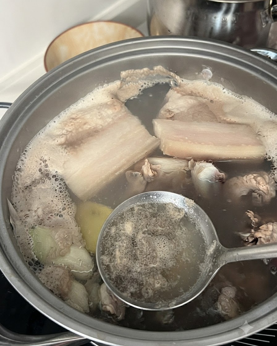Ein Schaumlöffel, der grauen Schaum und Verunreinigungen aus kochendem Wasser in einem Topf mit Schweinerippchen abschöpft.