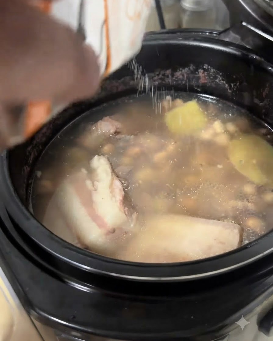 Salz wird aus einer weißen Packung in einen köchelnden Topf mit Schweinerippchen- und Erdnusssuppe geschüttet.