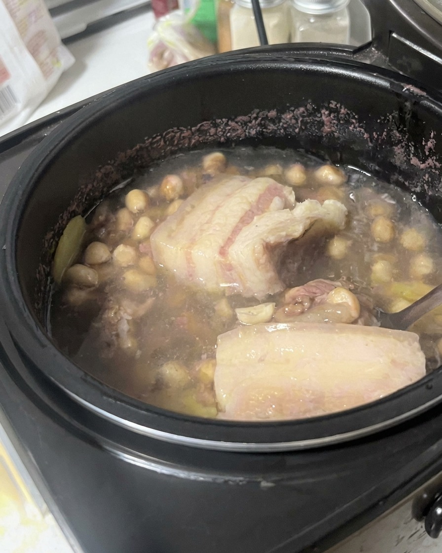 Schweinebauch wird mit einem Löffel in der Brühemischung angehoben und untersucht.