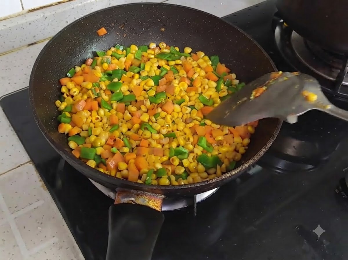 Eine Pfanne gefüllt mit buntem, gewürfeltem Mais, Karotten und grüner Paprika wird mit einem Spatel geschwenkt.