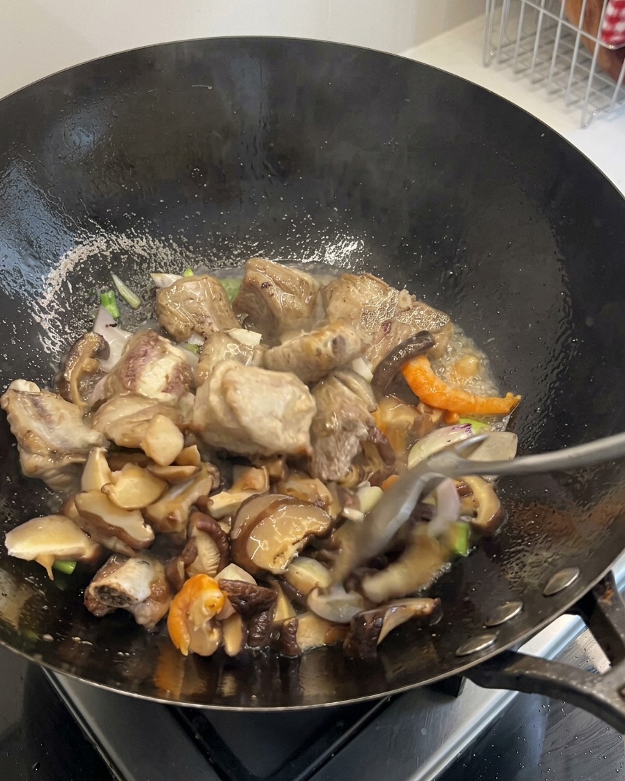 Gewürfelte Karotten und Maiskörner werden unter den brutzelnden Inhalt des Woks gemischt.