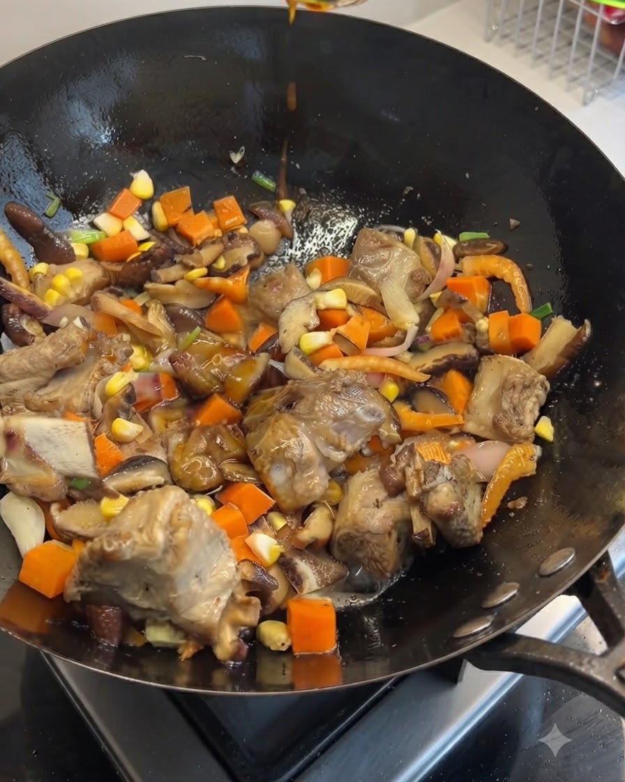 Dunkle und helle Sojasauce werden von oben in einen mit Schweinerippchen, Karotten, Pilzen und Mais gefüllten Wok geträufelt.
