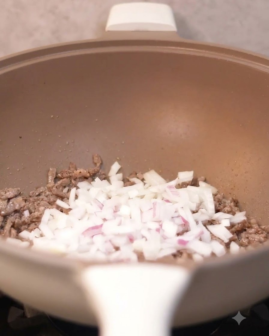 Gewürfelte Zwiebeln werden in den Wok zu den gebratenen Rindfleischstücken gegeben.