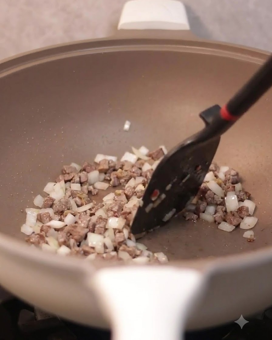 Ein Spatel rührt Rührei gemischt mit Rindfleisch und Zwiebeln in einer Bratpfanne um.