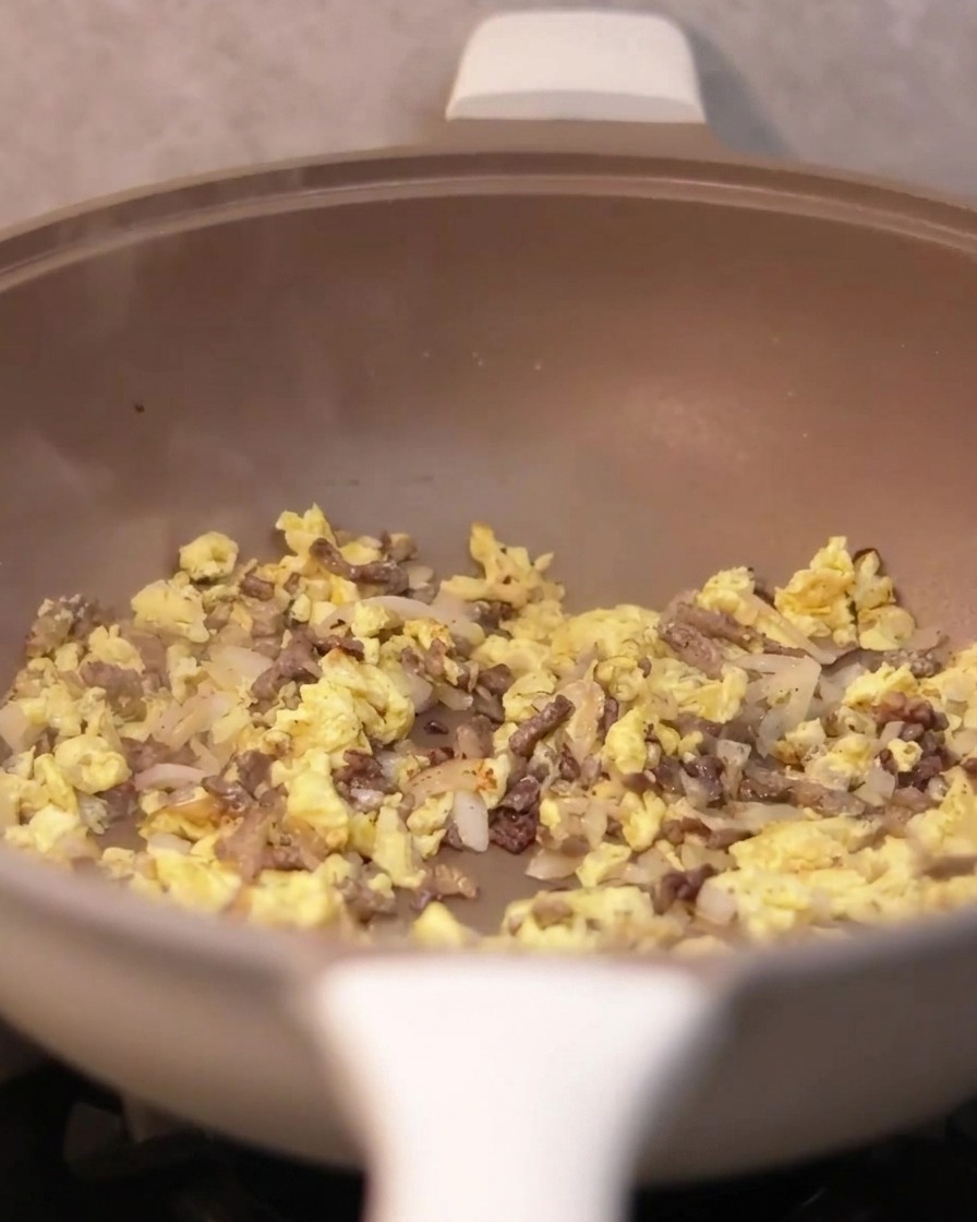 Trüffelsauce wird mit einem Löffel in die Pfanne mit Rindfleisch, Zwiebeln und Eiern gegeben.
