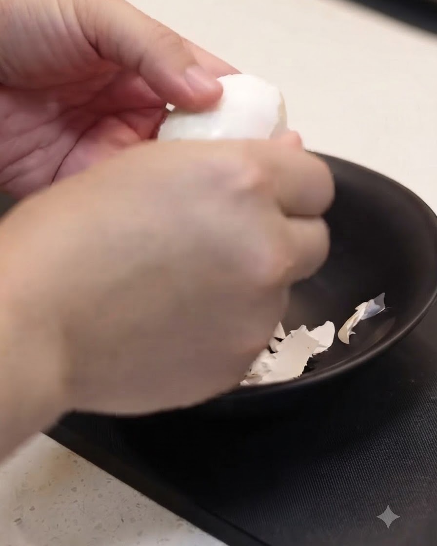 Ein gekochtes Ei wird über einer schwarzen Schüssel vorsichtig mit der Hand geschält.