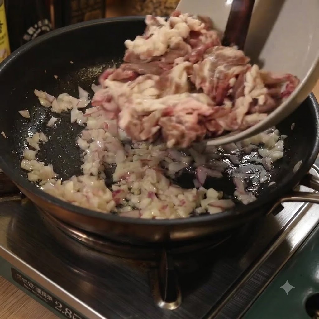 Dünne Rindfleischstreifen werden aus einer Schüssel in eine Bratpfanne mit angebratenen Zwiebeln und Knoblauch gegeben.