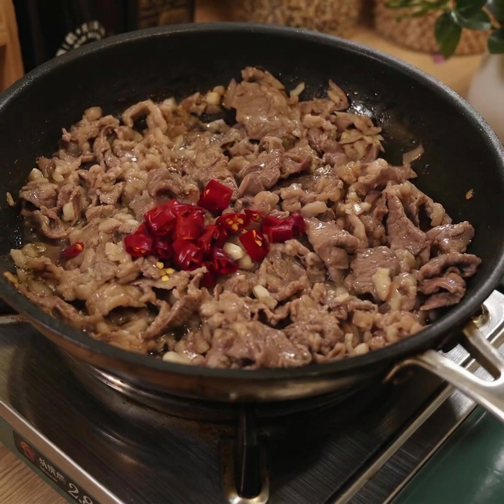 Gekochte Spaghetti-Nudeln werden in eine Pfanne mit Rindfleisch und in Scheiben geschnittenen roten Chilischoten gegeben.
