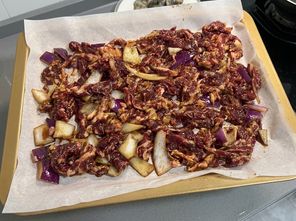 Mariniertes Rindfleisch und Zwiebelscheiben gleichmäßig auf einem mit Backpapier ausgelegten Backblech verteilt.