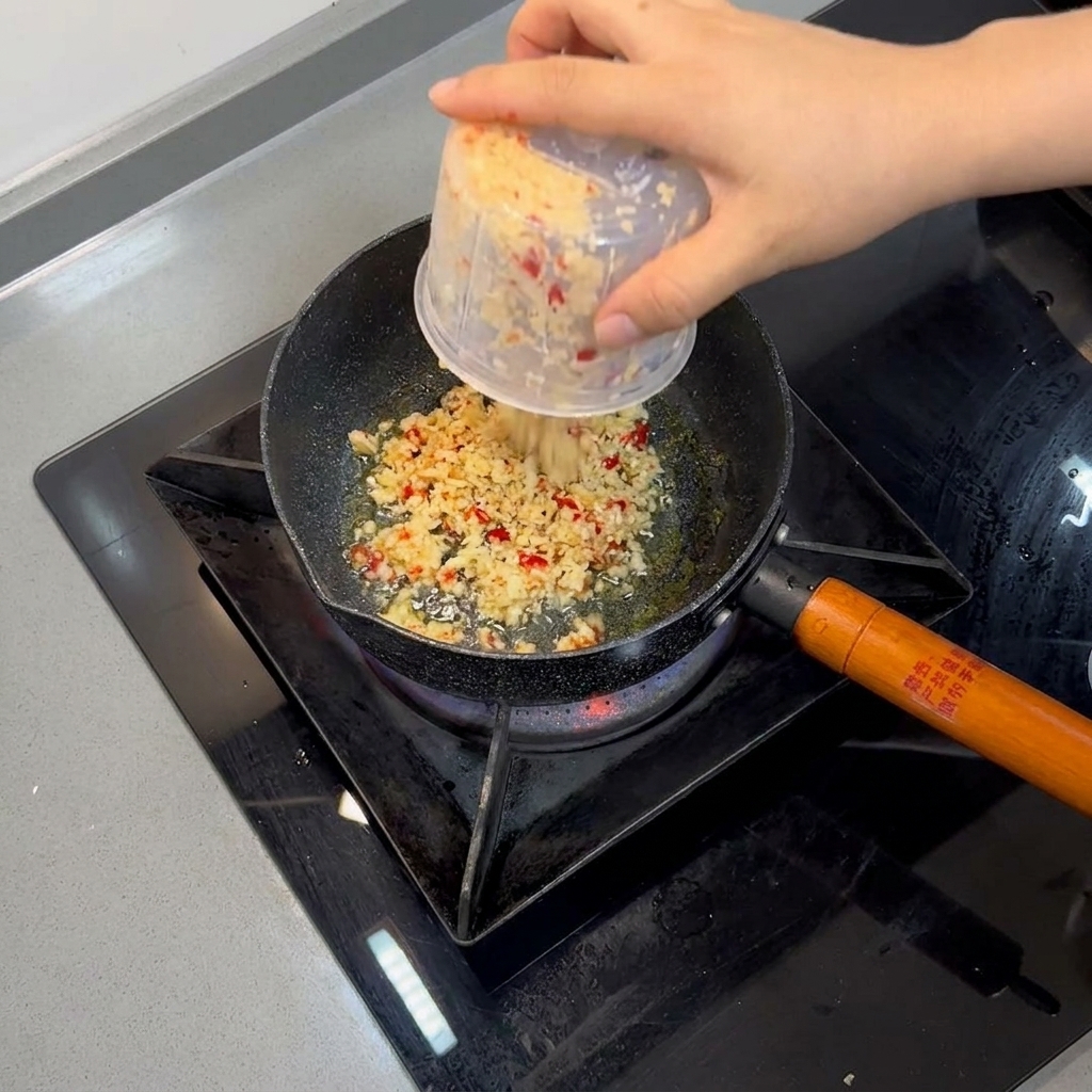 Fein gehackter Knoblauch und rote Chilis braten in heißem Öl in einer kleinen Pfanne.