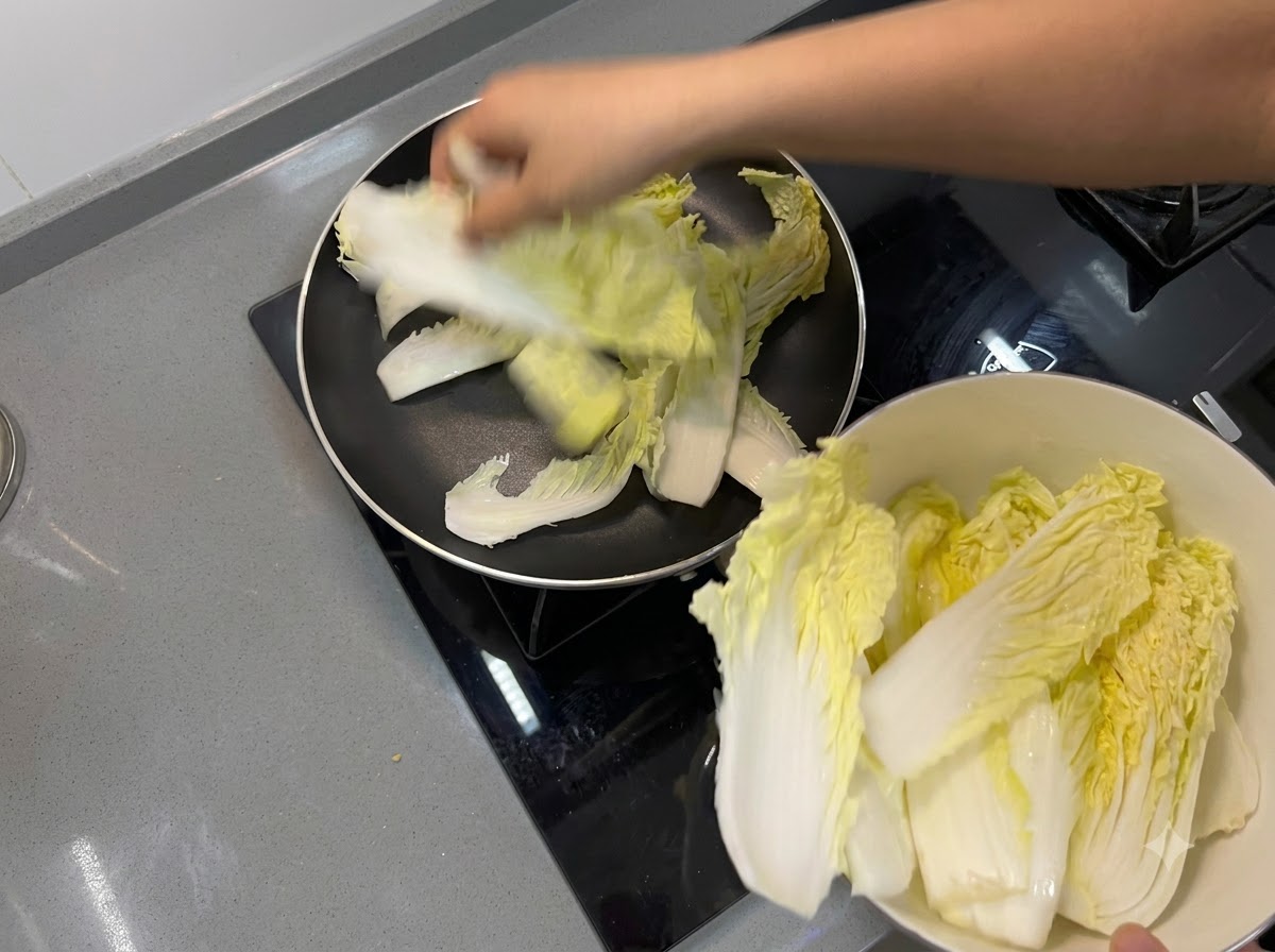 Chinakohlblätter werden so ausgelegt, dass sie eine Bodenschicht in einer Bratpfanne bilden.