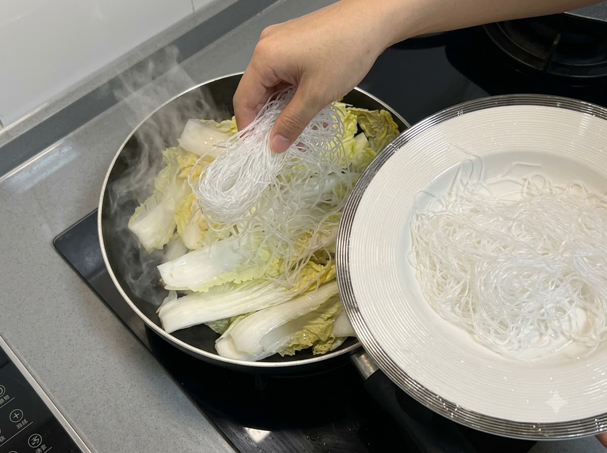 Glasnudeln werden oben auf den Chinakohl in der Pfanne gelegt.