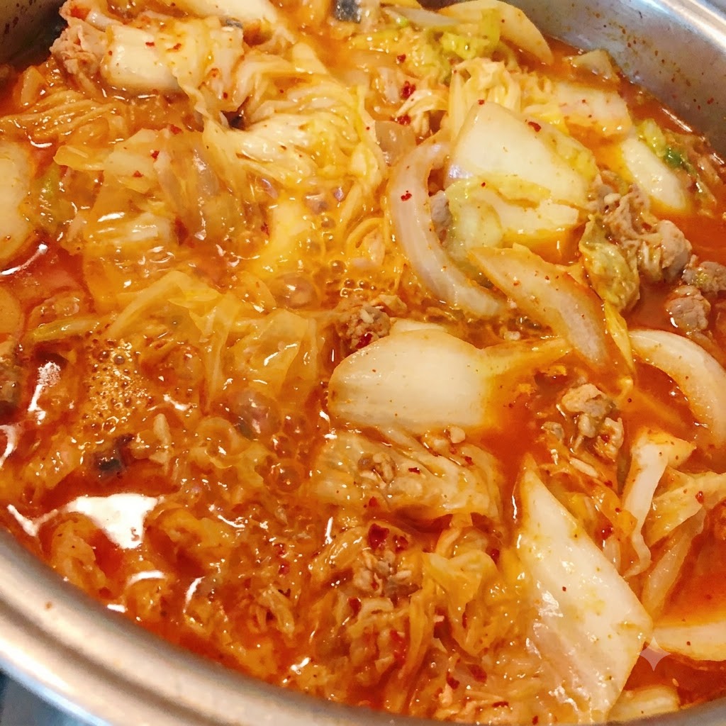 Chilipulver wird in den köchelnden Kimchi-Thunfisch-Eintopf gegeben.