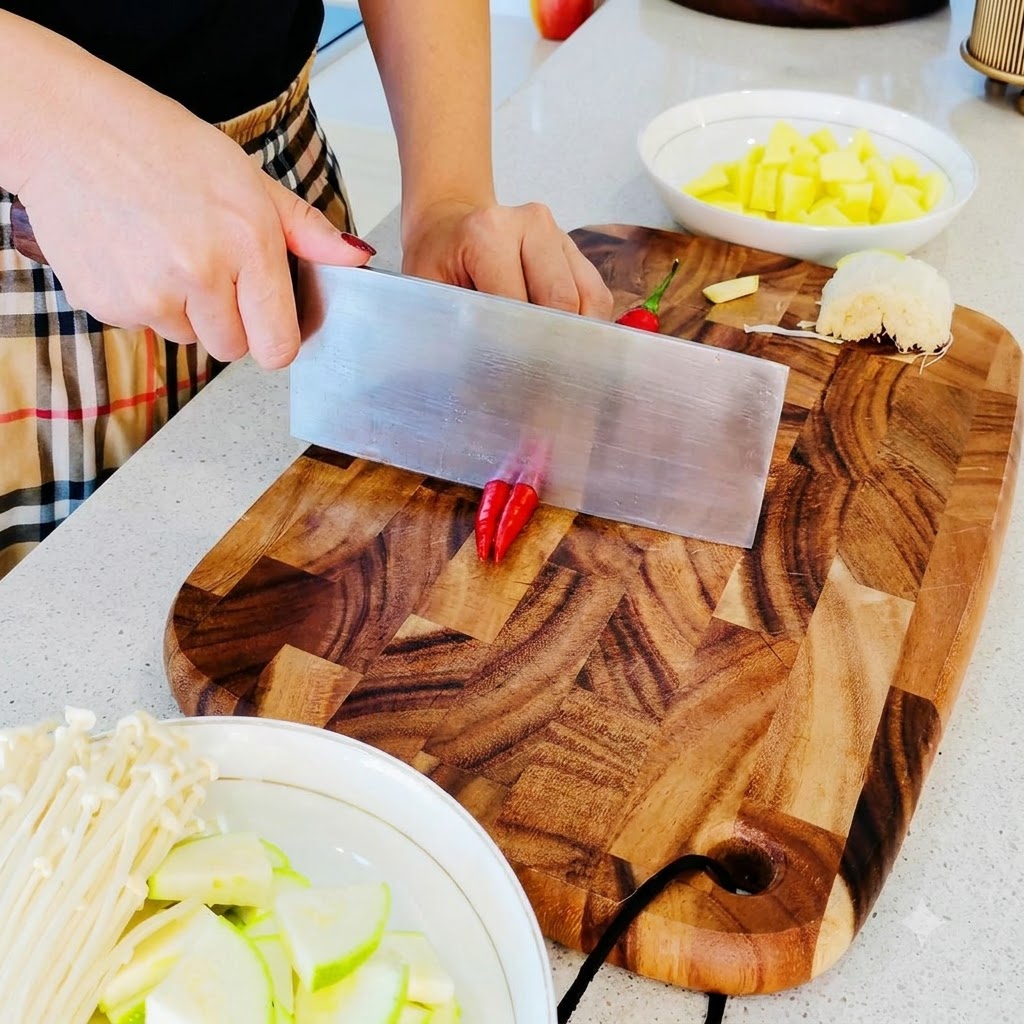Kleine rote Chilischoten werden auf einem Holzschneidebrett in feine Stücke gehackt.