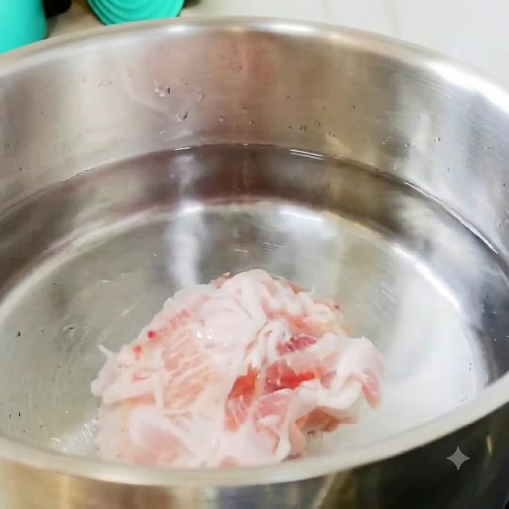 Geschnittener Schweinebauch und Kartoffelstücke liegen in einem Edelstahltopf mit kaltem Wasser auf dem Herd.