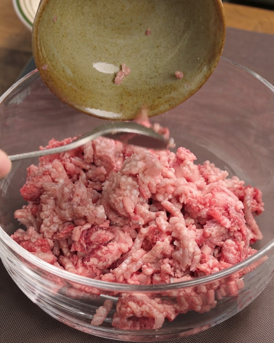 Eine Nahaufnahme einer weißen Zwiebel, die auf einer braunen Schneidematte mit einem silbernen Chefkochmesser gewürfelt wird.