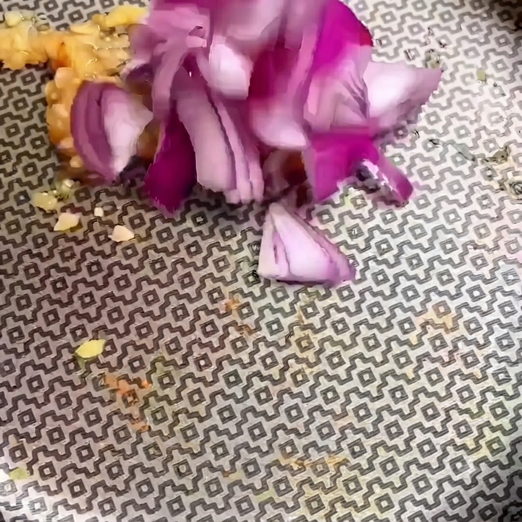 Fein gehackte rote Zwiebelstücke werden in einer gemusterten Pfanne zu gehacktem Knoblauch gegeben.