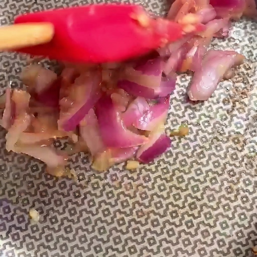 Ein roter Spatel mischt aktiv Zutaten in einer Kochpfanne.