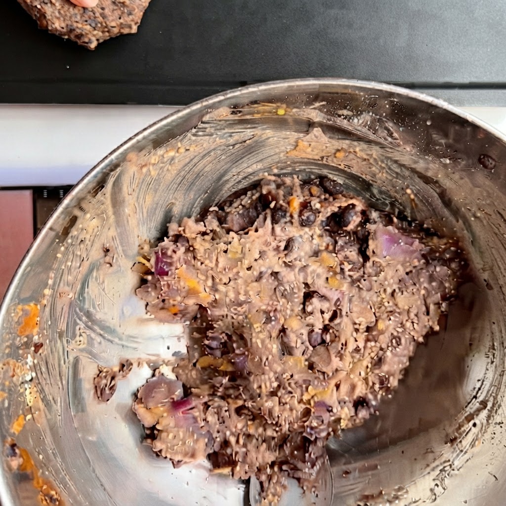 Mehrere geformte schwarze Bohnen Burger Patties säuberlich auf einem dunklen Backblech angeordnet.