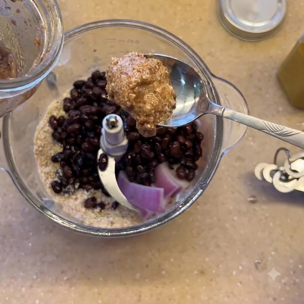 Ein Löffel Mandelmus wird über dem Mixer mit schwarzen Bohnen und roten Zwiebeln gehalten.