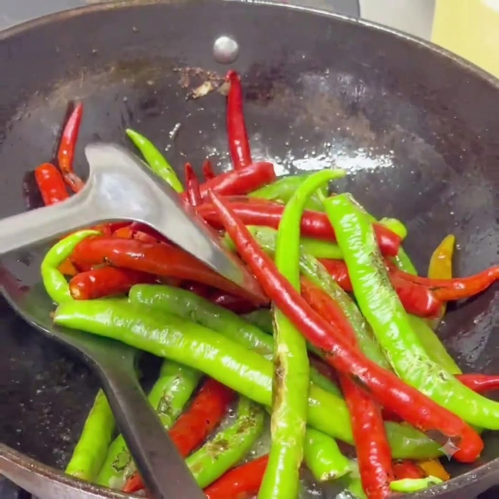 Geröstete Chilischoten werden mit einem Spatel in einem mit gewürztem Öl gefüllten Wok gebraten.