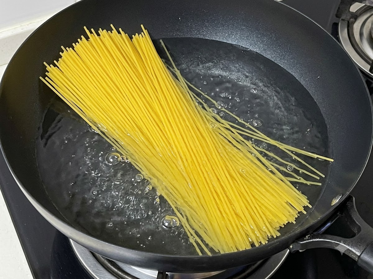 Ein Bündel trockener Spaghettinudeln wird in einen Topf mit kochendem Wasser gegeben.