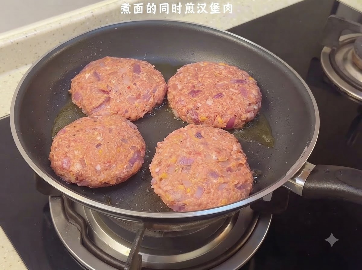 Vier rohe Hamburger-Patties brutzeln in einer Bratpfanne auf dem Herd.