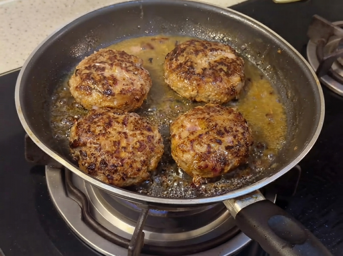 Hamburger-Patties garen in einer Pfanne, während die flüssigen Saucenzutaten beginnen sich zu verbinden.