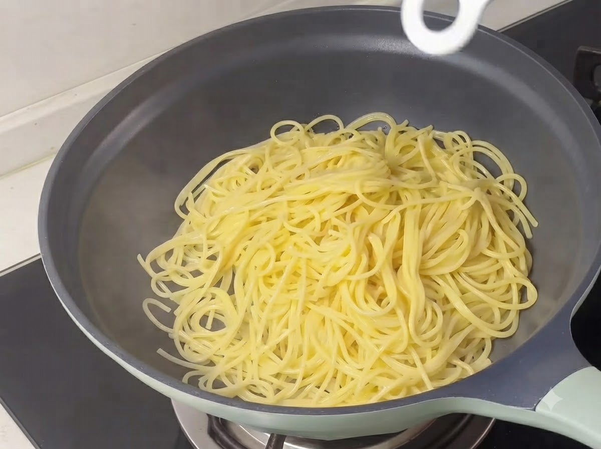 Gekochte gelbe Spaghettistränge liegen in einer Pfanne.