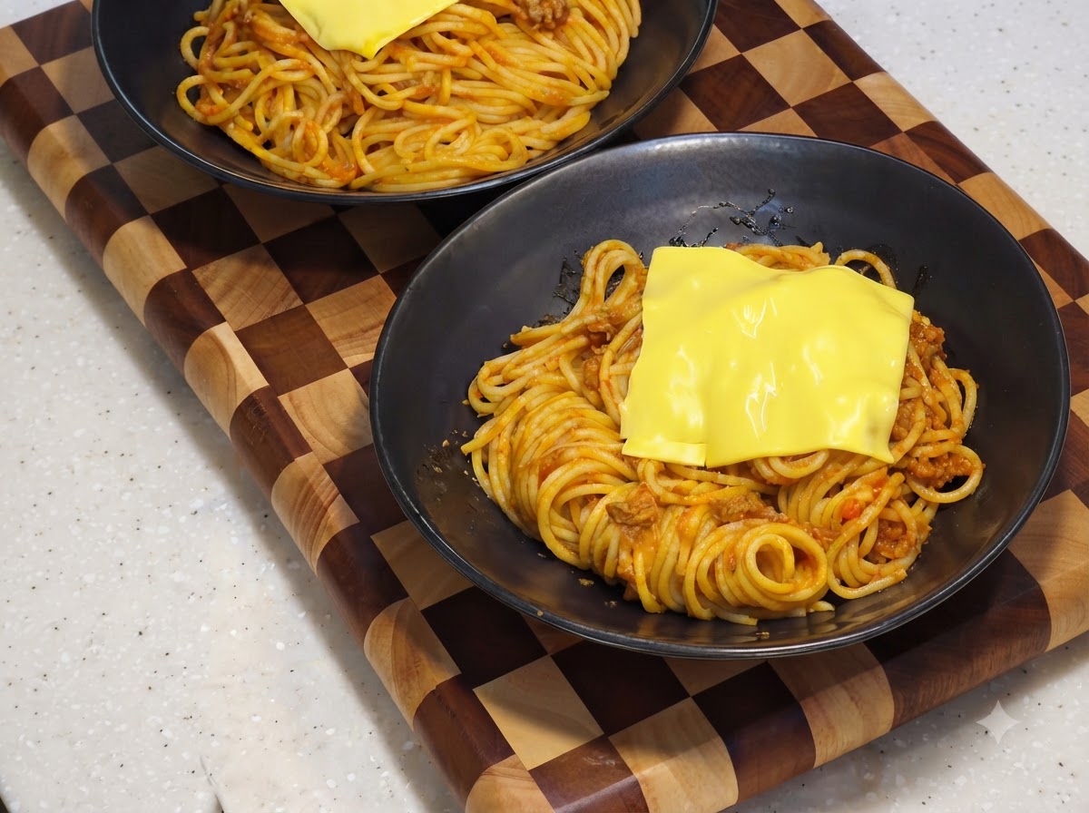 Eine gelbe Käsescheibe schmilzt über dem Spaghetti-Bett in einer schwarzen Servierschüssel.