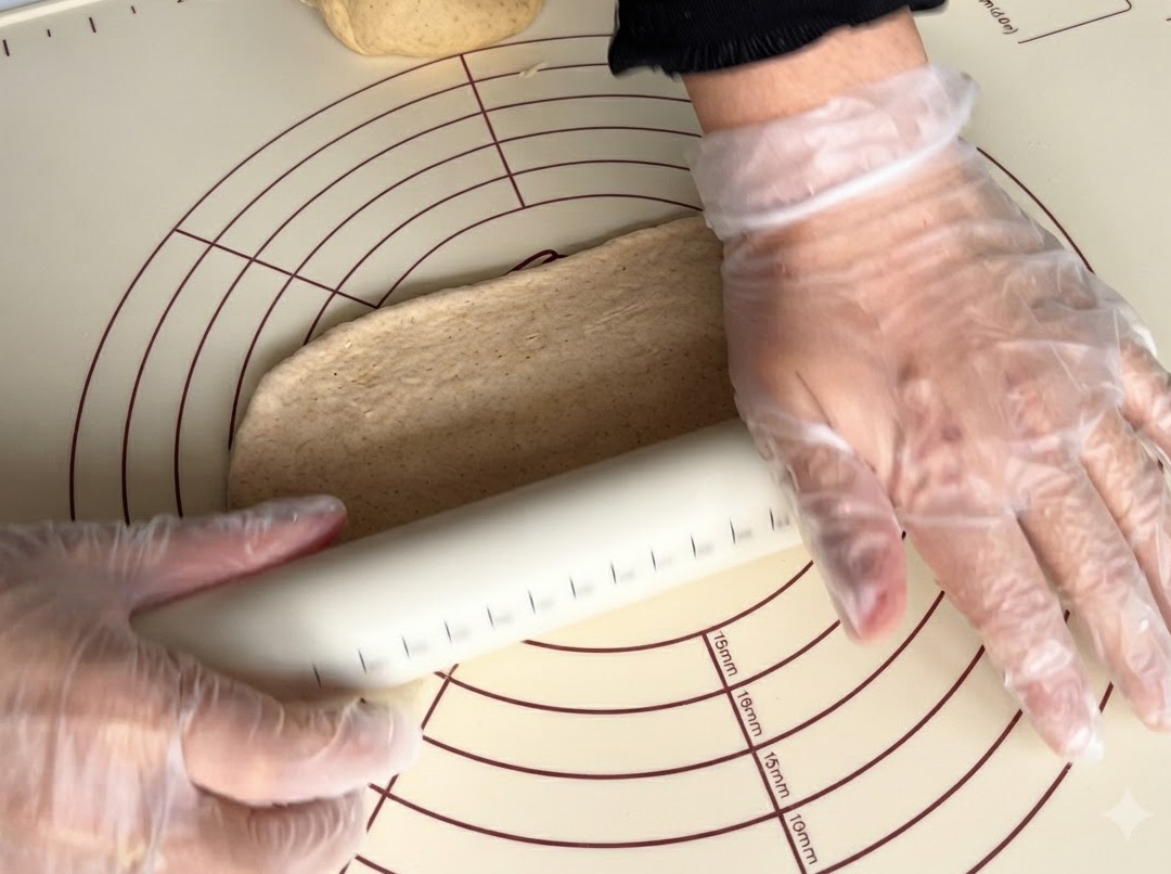Ein Nudelholz rollt ein Stück Vollkornteig auf einer Silikonmatte flach.