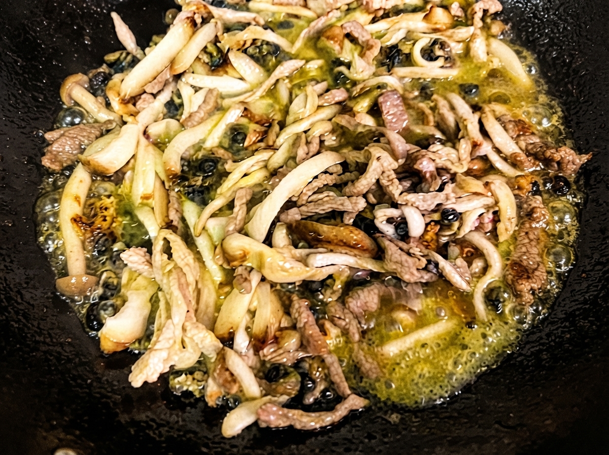 Fein geschnittene Shiitake-Pilze, Enoki-Pilze und Meeresschnecken braten in heißem Öl in einem schwarzen Wok an.