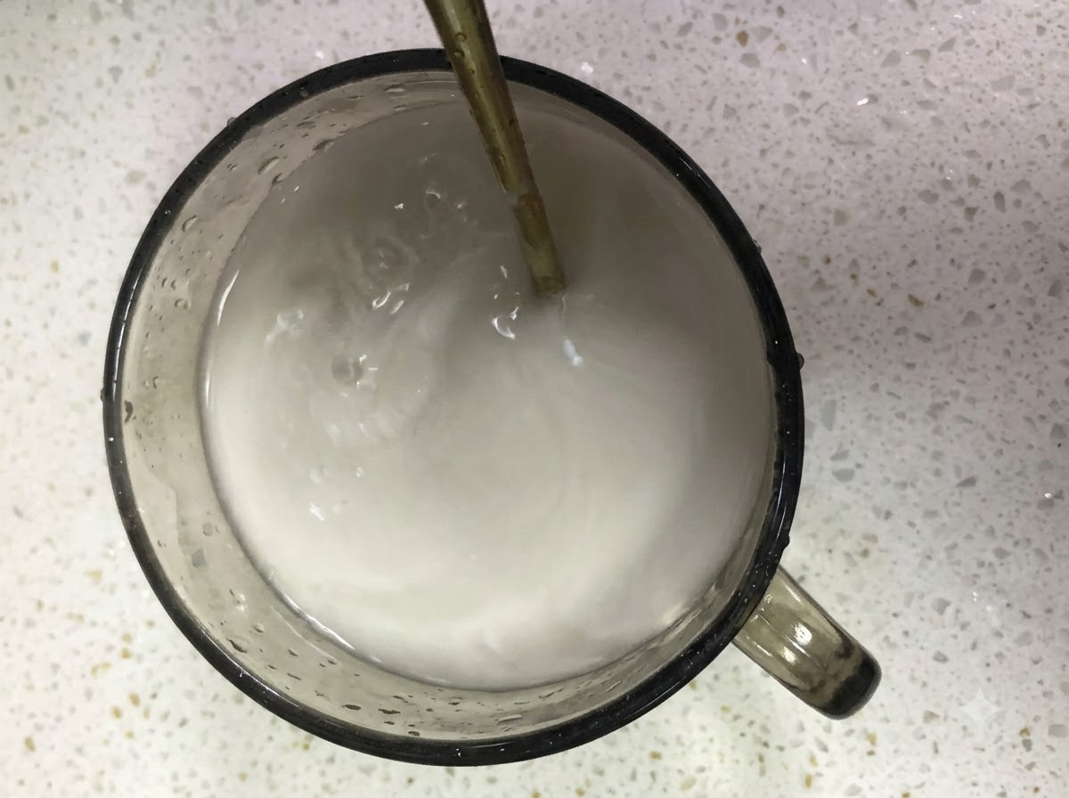 Reine Süßkartoffelstärke und Wasser werden in einem Glasbecher mit einem Löffel verrührt.