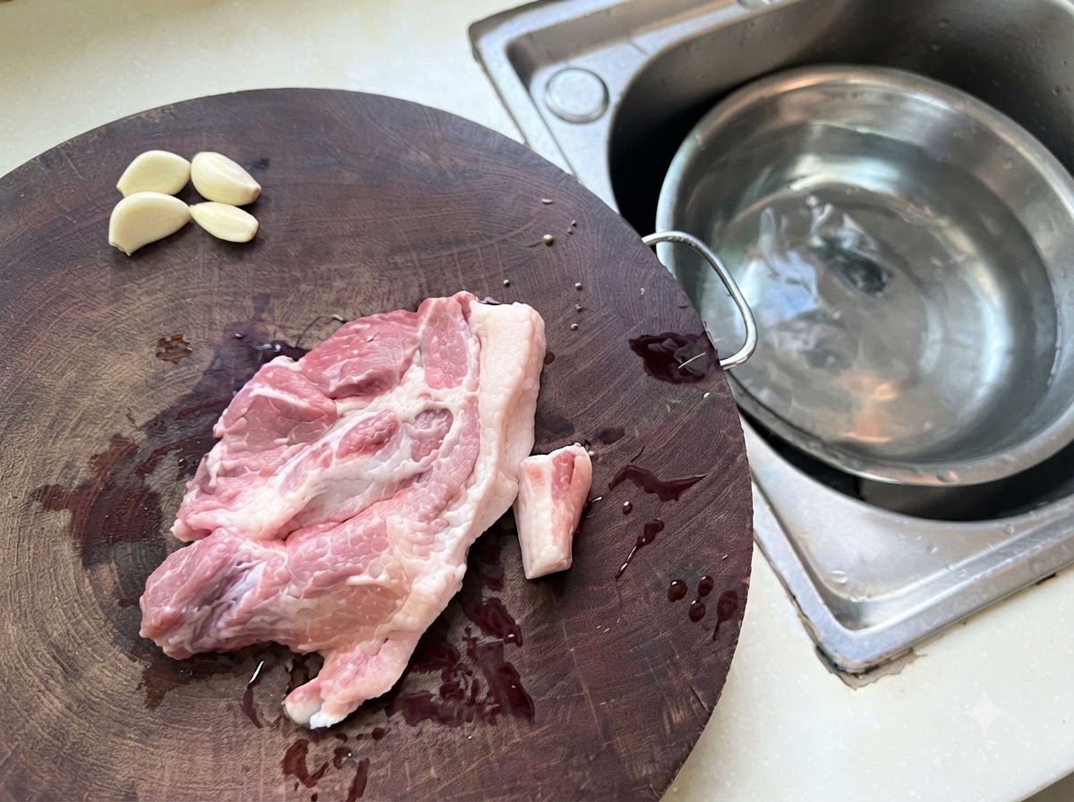 Hackfleisch und Knoblauchstücke verteilt auf einem Holzschneidebrett neben einer Metallschüssel mit Wasser.